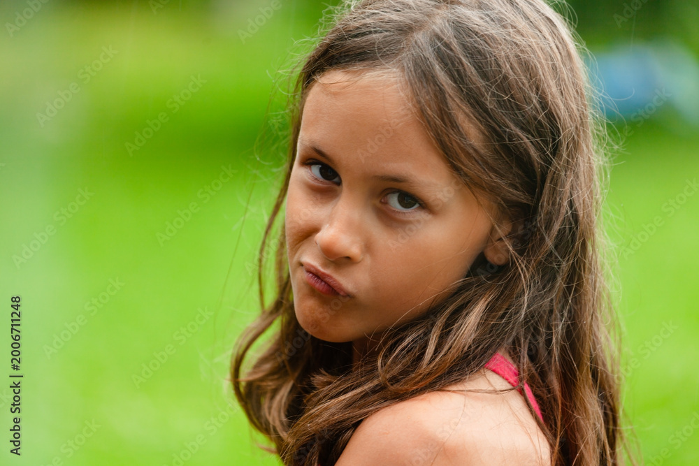 Fototapeta premium grimace child gazes in close-up portrait revealing energy, enthusiasm and fun. Young girl shows funny expression with thoughtfulness and a sly grin. Kid expresses emotions