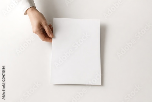 A person's hand holding a blank white sheet of paper against a clean white background.