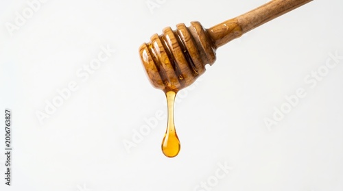 A wooden honey dipper coated in golden honey lets a thick drop fall in a long strand against a white background.