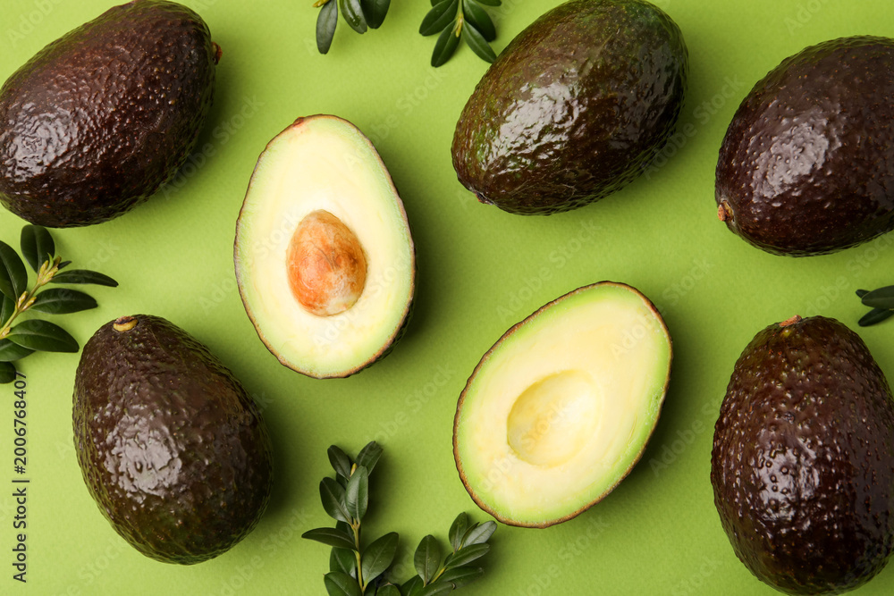 Fototapeta premium Fresh ripe avocados and leaves on green background, flat lay