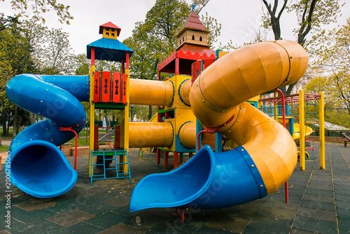 Imaginative children's play area with a large blue yellow spiral slide, colorful castle towers, tunnels, and climbing frames in a green park setting.