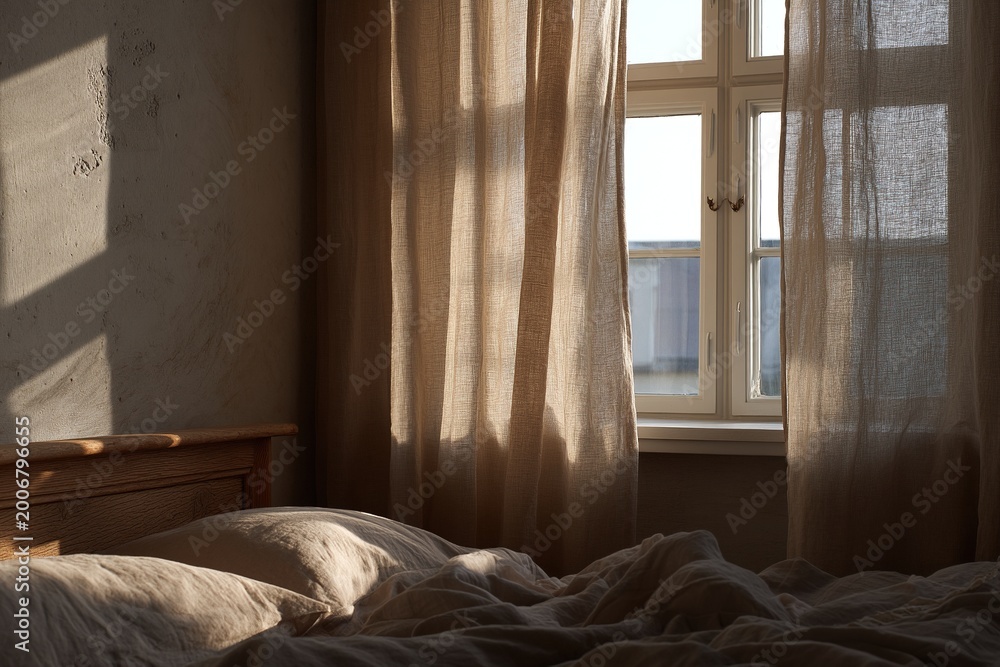Fototapeta premium Sunlit bedroom with soft linen bedding and window curtains creating warm morning atmosphere