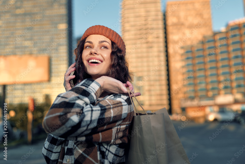 Fototapeta premium Woman shopping on city street, phone to ear and smile in golden hour glow, candid lifestyle portrait with authenticity, mindful living warmth and emotional storytelling in urban fashion scene.