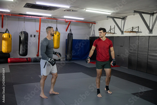 Diverse male training partners sparring on interlocking mats in martial arts gym wearing MMA gloves