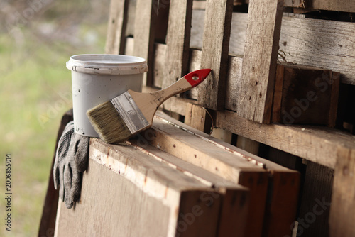 Painting set: brush, gloves and small white bucket with paint or varnish on wooden background. Workshop. Repair and construction concept. Painting tools on wooden background. Close-up of tools