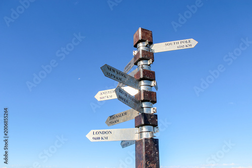 Direction signpost pointing world cities blue sky background. Metal arrows indicating global travel destinations distance during sunny day suitable for tourism and adventure navigation concepts
