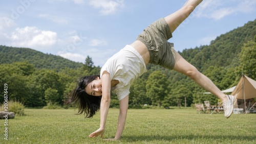 キャンプ場の芝生で元気に側転をして遊ぶ女性 #2006876439