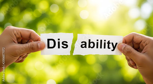 Human hands holding two torn pieces of white paper with the word disability written on them to demonstrate the concept of removing social barriers today