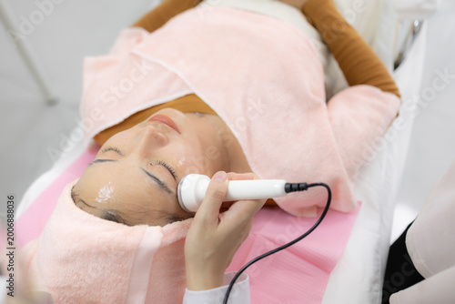 Young woman relaxes during facial treatment. Professional hands gently cleanse her eyes. Soft pink towels frame her serene expression. Relaxed posture suggests comfort and care
