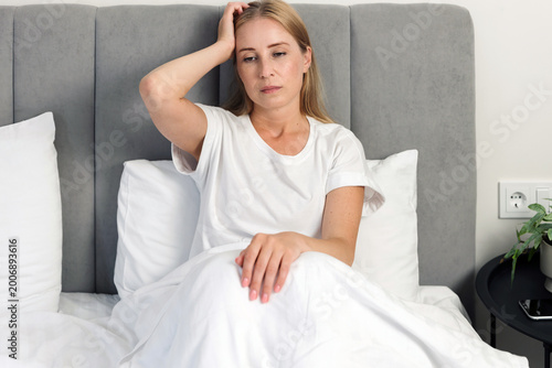 Woman feeling headache sitting in bed at home