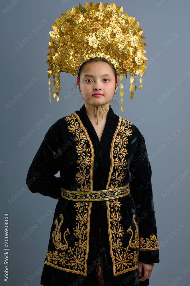Fototapeta premium Young Indonesian Asian Girl Portrait Wearing Ornate Gold Headdress and Embroidered Traditional Dress in Studio