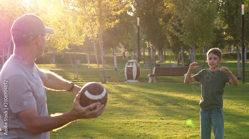 Father and son playing American football in park at sunset, passing ball and running on grass in warm golden light. Coaching, mentorship and active parenting. Healthy childhood and outdoor lifestyle.