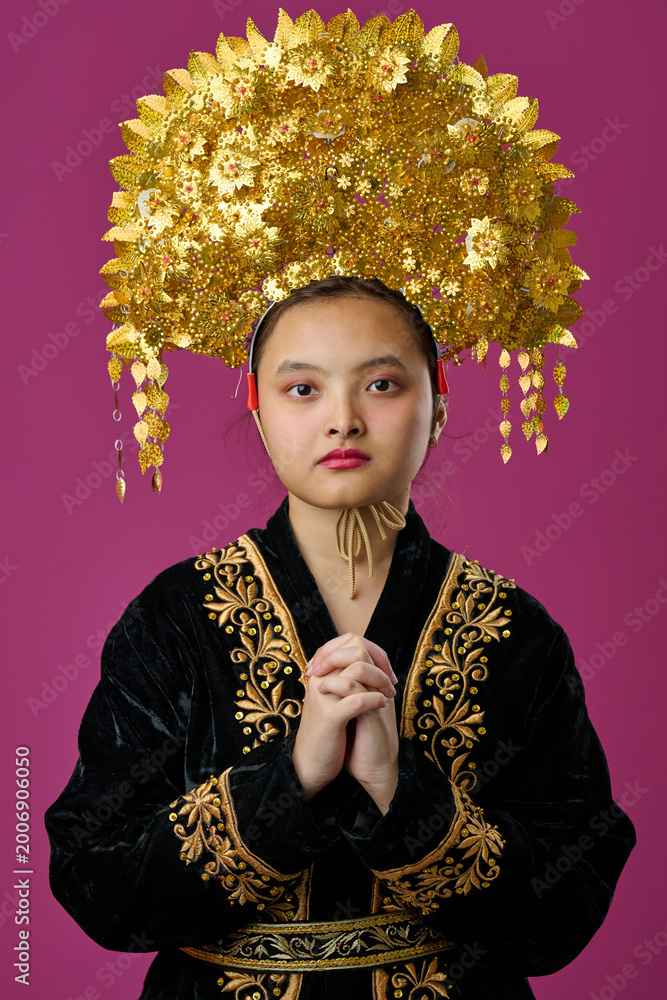 Fototapeta premium Young Indonesian Asian Woman Wearing Ornate Gold Headdress And Embroidered Black Traditional Costume Portrait