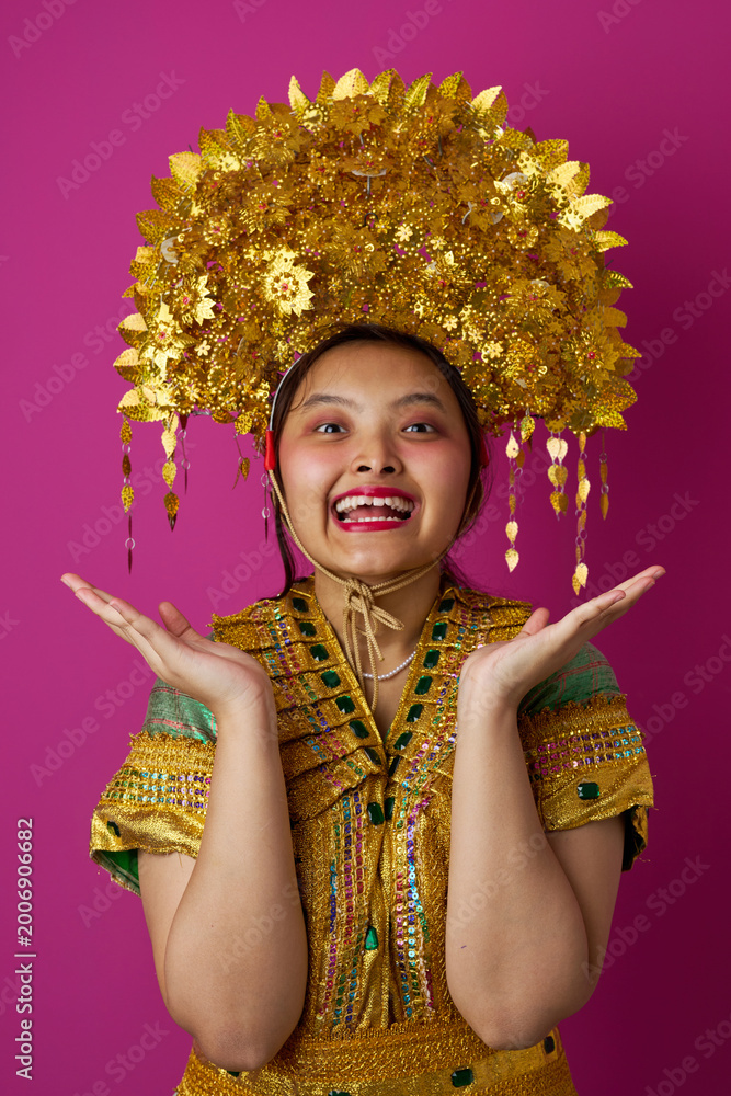 Fototapeta premium Young Indonesian Asian Woman in Golden Traditional Headdress and Embellished Costume Celebrating Cultural Festival