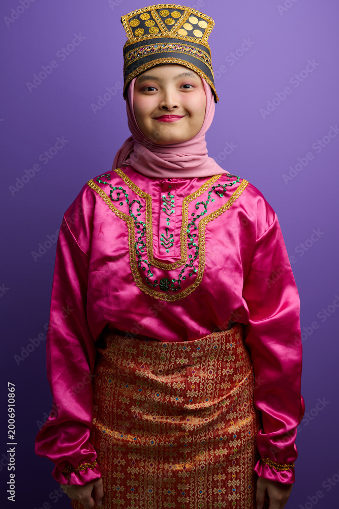 Obraz premium Young Indonesian Asian Girl in Traditional Malay Costume and Hijab Posing Against Purple Background