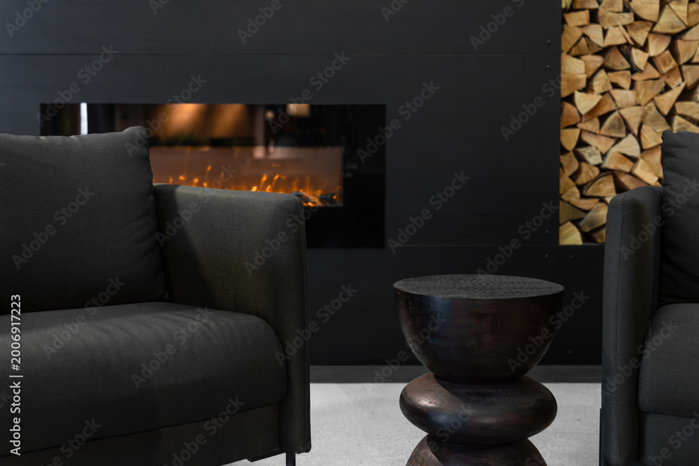 Fototapeta premium Living room interior with fireplace and logs. Modern furniture and decorative side table.