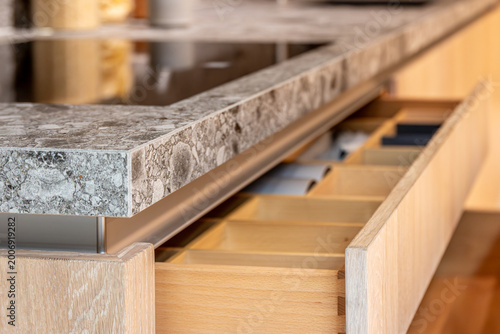 Organized kitchen island drawer made of wood. Detailed view of modern kitchen furniture.