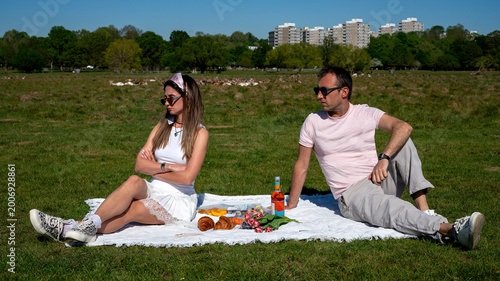 Photos Unset couple sitting apart on picnic blanket with crossed arms and resentful loo