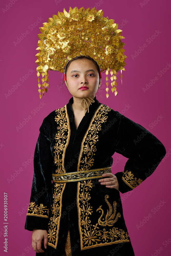 Fototapeta premium Portrait Of Young Indonesian Asian Woman Wearing Traditional Gold Headdress And Embroidered Black Robe