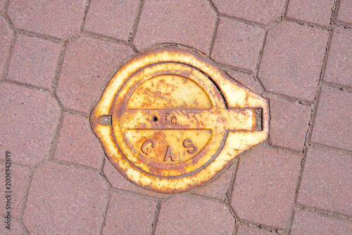 Fényképezés Rusty gas cover on textured brick pavement under bright sunlight