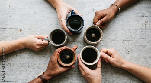 Overhead shot of diverse hands holding coffee cups in a circular composition, symbolizing teamwork, community and connection, neutral background with copy space, soft diffused lighting