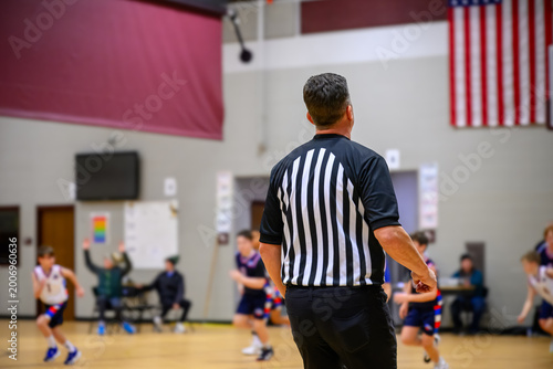 Basketball game in school gym with referee overseeing young players during match in early evening hours