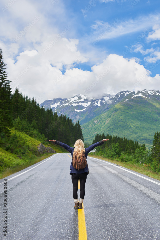 Fototapeta premium Backpack, woman and arms up on road with mountain view, sightseeing and travel exploration for vacation. Back, person and adventure outdoor with scenery for winter holiday, hiking trip and freedom.