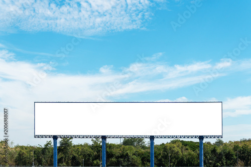 Wide, white empty billboard stands tall against a bright blue sky with light clouds. Perfect for advertising placement mockups, marketing displays, and outdoor brand promotion.