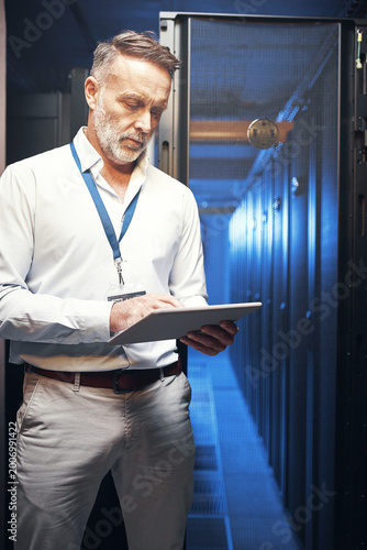 Engineer, man and typing on tablet in server room for maintenance, diagnostics and IT solution. Technician, mature person and tech in data center for system backup, troubleshooting and cybersecurity