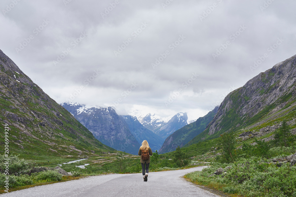 Fototapeta premium Mountain, backpacking and woman on road for journey, mockup space and fresh air on adventure or travel. Outdoor, person and hiking on weekend, exploration and trekking with view of valley and scenery
