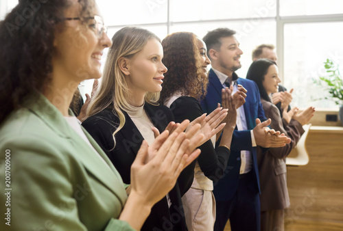 Business team professionals applauding success during meeting. Diverse colleagues smile and offer applause. Ideal for corporate training and celebration. Clear concept of teamwork and motivation.