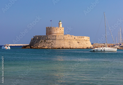 Medieval fortress with lighthouse and yacht in Mandraki harbor Rhodes Greece