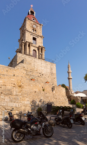 Clock tower above stone walls with scooters in old town of Rhodes Greece