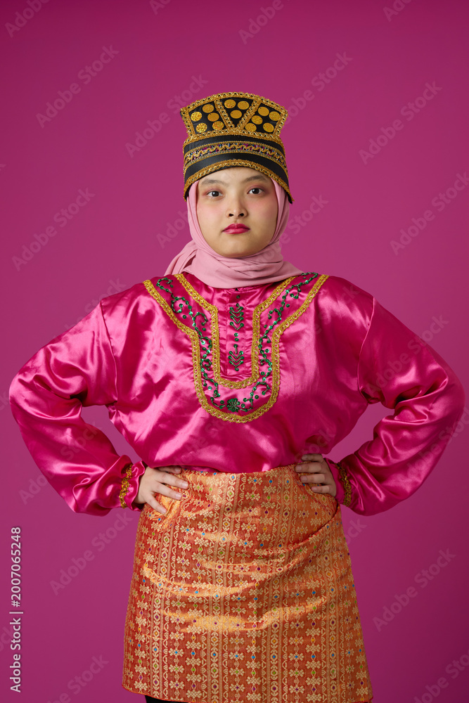 Fototapeta premium Confident Indonesian Asian Woman in Bright Pink Traditional Costume and Hijab Wearing Ornate Gold Headdress