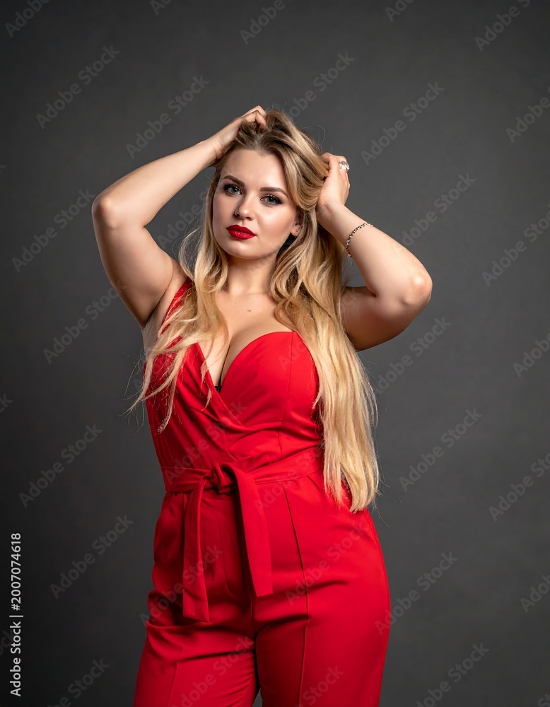 Fototapeta premium Attractive woman in red jumpsuit poses, hand over her head