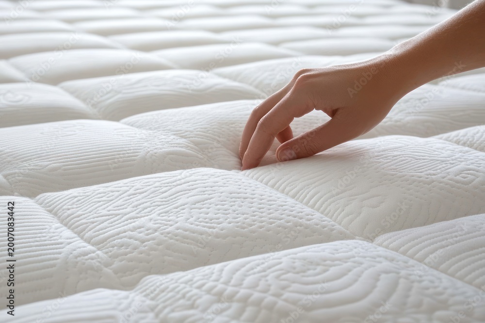 Fototapeta premium hand pressing into quilted white mattress surface creating a soft indentation and evoking comfort and relaxation