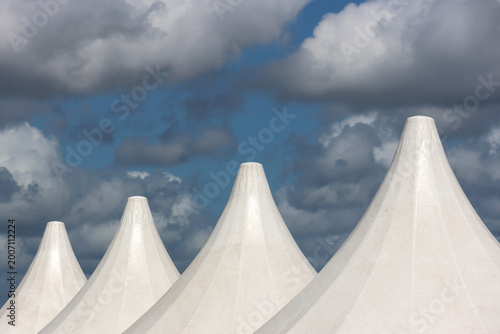 Fotografía Row of white peaked fabric roof structures against a blue cloudy sky