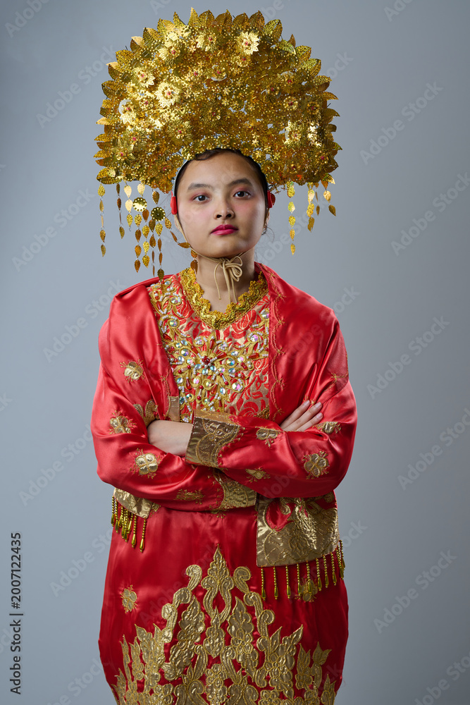 Naklejka premium Young Indonesian Asian Woman Wearing Ornate Gold Headdress and Red Traditional Costume Portrait