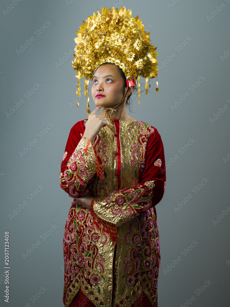Fototapeta premium Portrait of Indonesian Asian Woman in Traditional Red and Gold Costume Wearing Ornate Golden Headdress