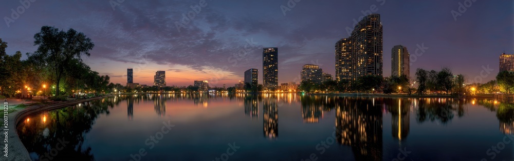 Fototapeta premium Panoramic view of a modern city skyline reflected in a calm lake at dusk.
