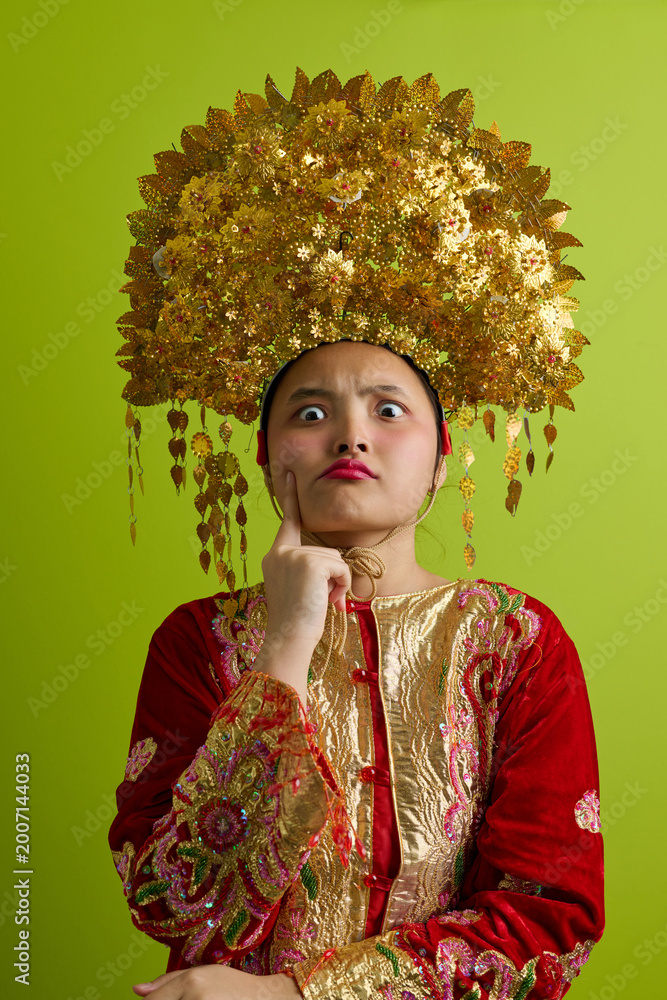Fototapeta premium Portrait Of A Young Indonesian Asian Girl Wearing A Golden Headdress And Traditional Red Costume With Playful Expression