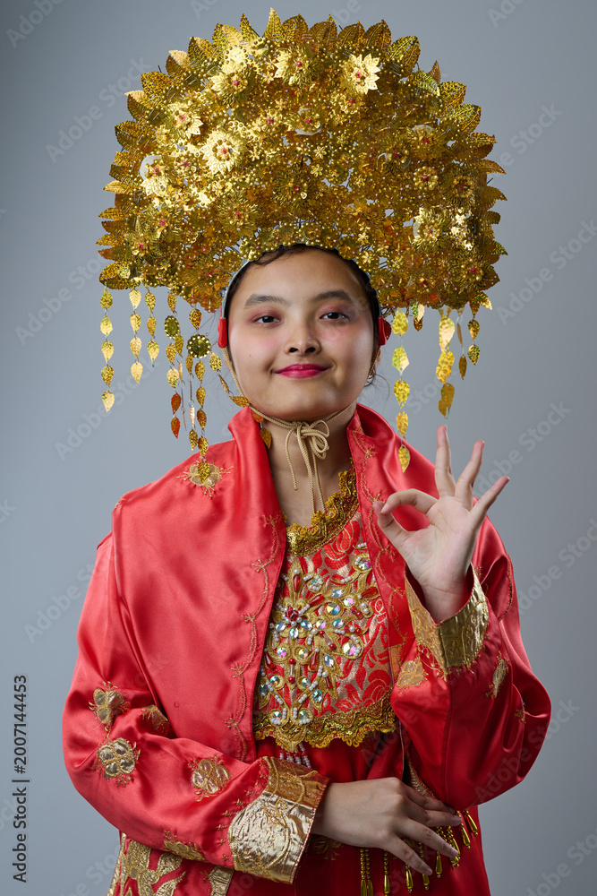 Fototapeta premium Young Indonesian Asian Girl in Ornate Gold Headdress and Red Traditional Costume Smiling in Portrait