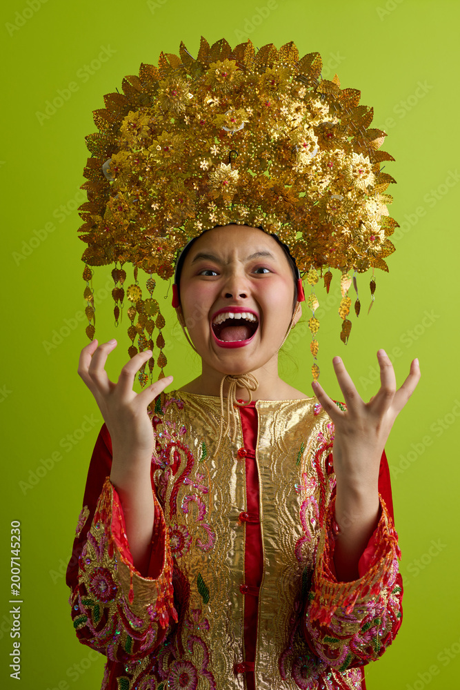 Obraz premium Young Indonesian Asian Girl Wearing Ornate Gold Headdress and Traditional Embroidered Costume Screaming with Excitement