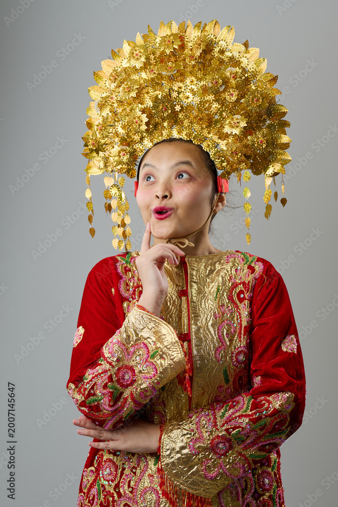 Obraz premium Young Indonesian Asian Girl in Gold Floral Headdress and Embroidered Red Traditional Costume Looking Surprised