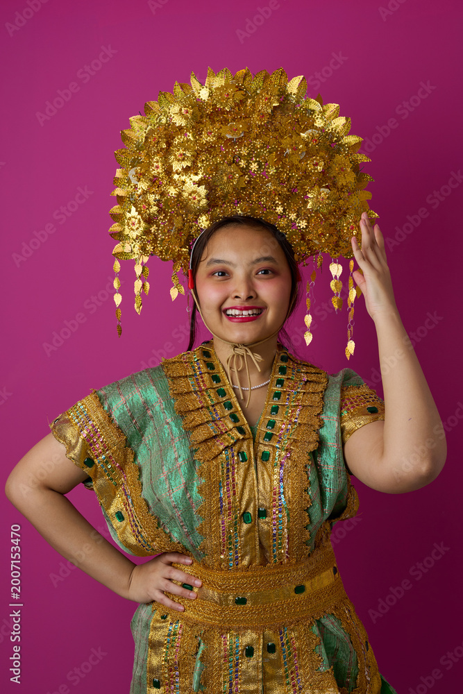Obraz premium Smiling Indonesian Asian Woman Wearing Ornate Gold Headdress And Traditional Embroidered Costume For Cultural Festival