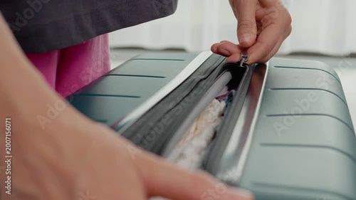 Hands are shown closing a suitcase filled with clothes for a trip. The action shows preparation and packing for a vacation or a journey.