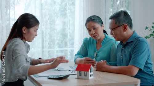 Professional financial advisor meeting with senior couple at home, discussing real estate investment, mortgage planning, and retirement finance with house model on table.