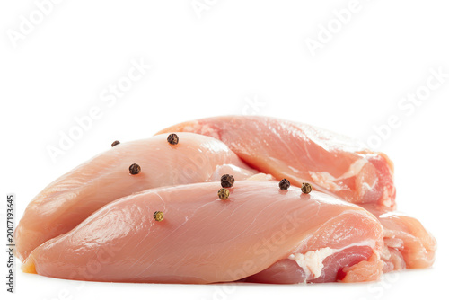 Raw fresh chicken breast fillets seasoned with whole black peppercorns on white background