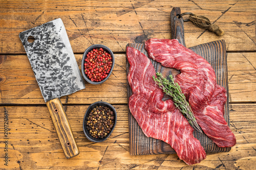 Fresh raw premium  beef meat steak slices with visible marbling on wooden surface with butcher knife and rosemary, ingredient for cooking grilling or barbecue