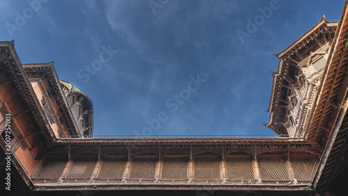 Ancient Newar architecture. A fragment of a temple with barred windows. Roofs against the blue sky. Beautiful wood carving. Nepal. Kathmandu. Durbar Square.